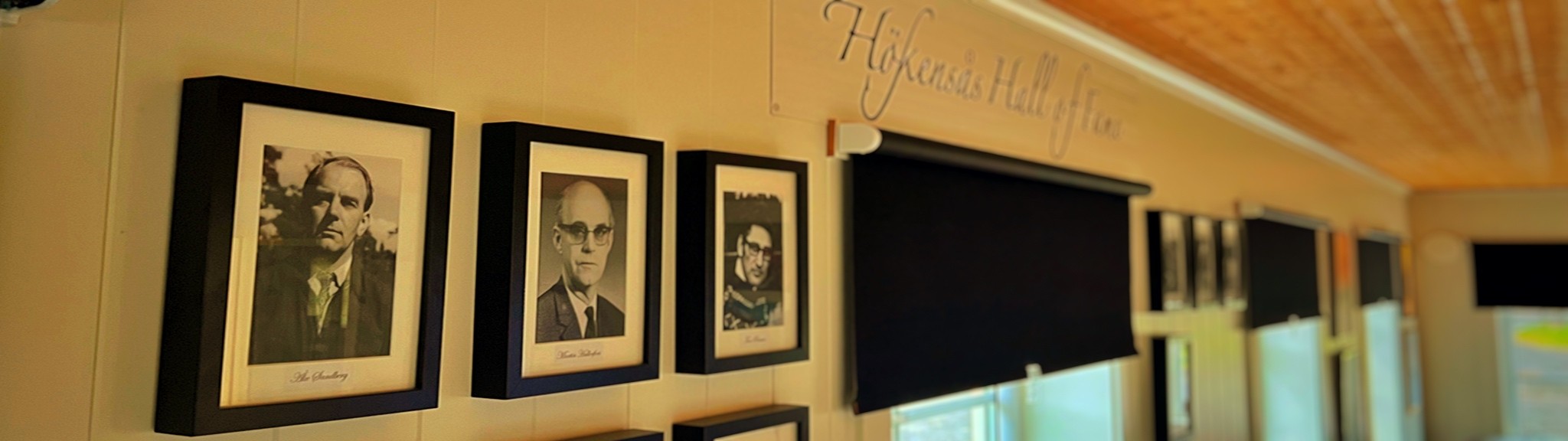 Vägg med svarta ramade porträtt och skylt Hökensås Hall of Fame