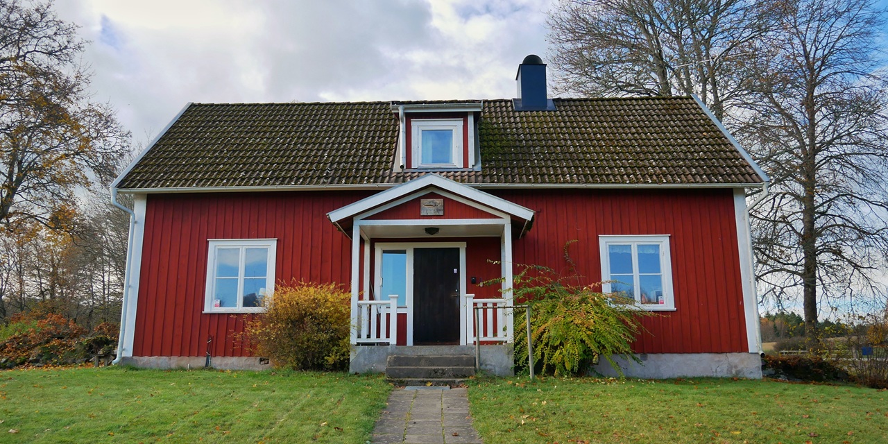 Röd trästuga med vit kant och grön gräsmatta i höstens ljus.